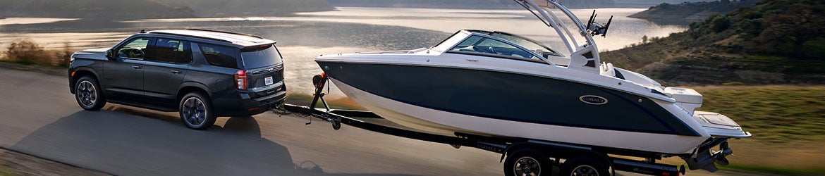 A Tahoe pulling a boat down the road along a lake.